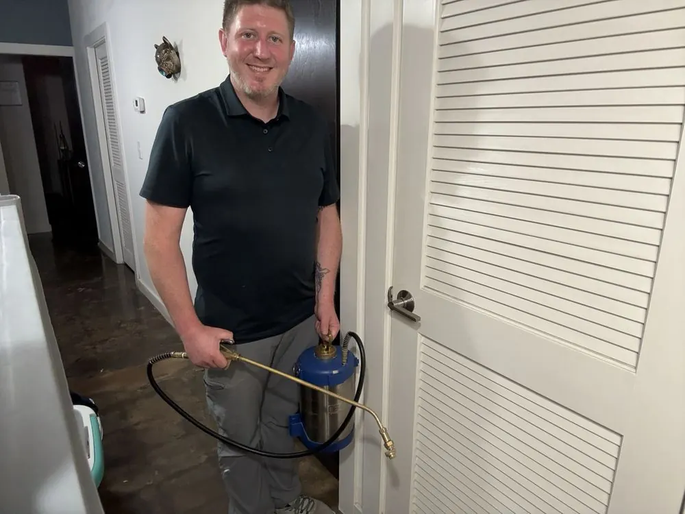 Chase, owner of Mill Mountain Pest Control, smiling with a pest-control sprayer